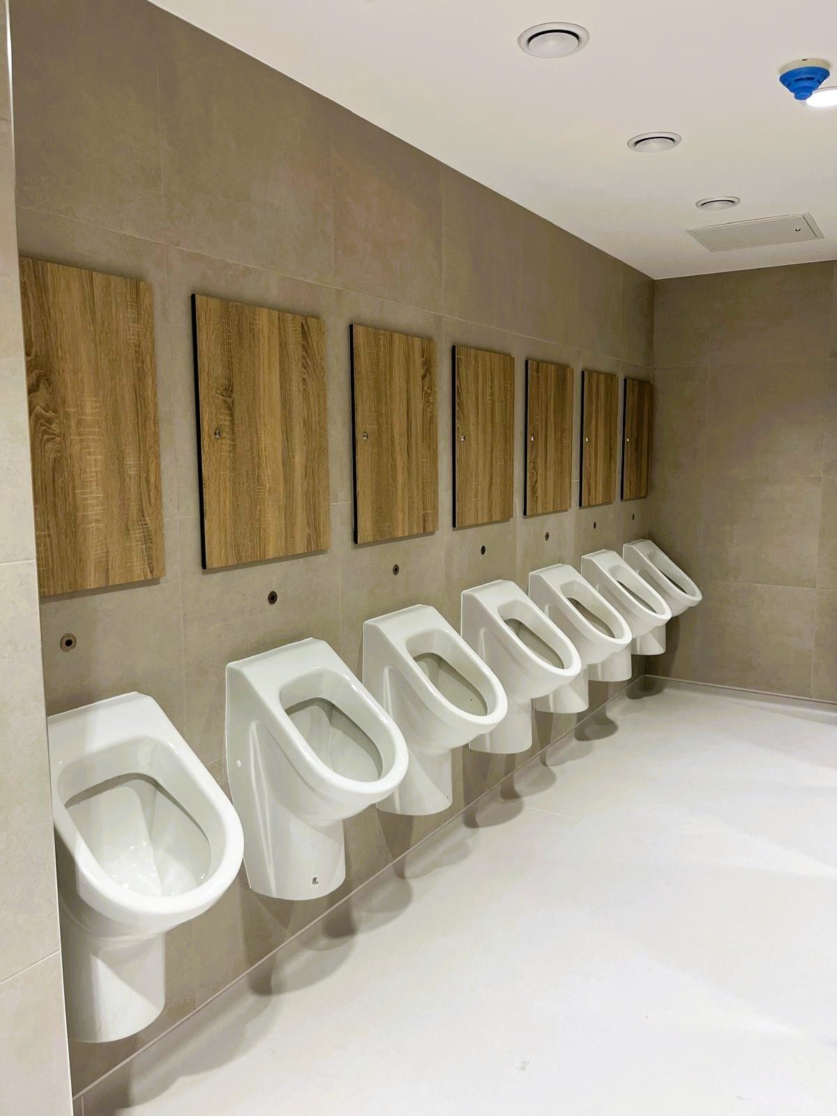 Wood-effect Mirage IPS duct panels above urinals in an airport washroom